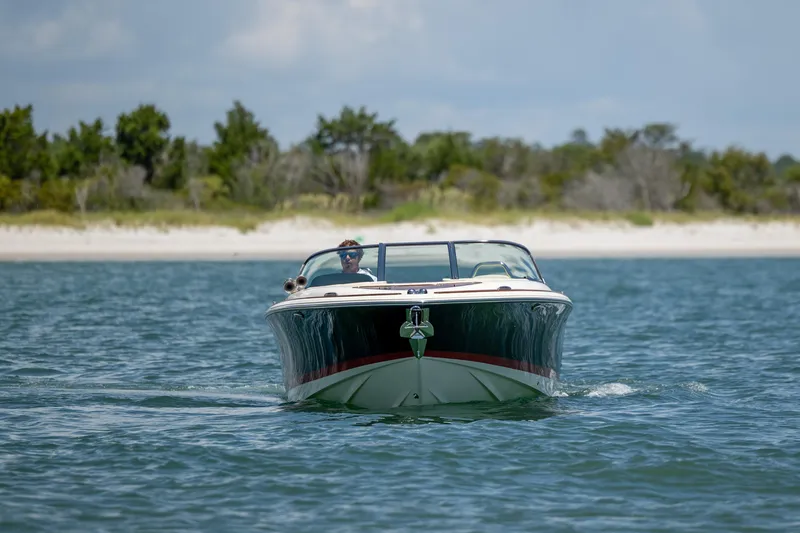 Slide: The Image of 2022 Chris-Craft Launch 27 boat cruising on calm water near a sandy beach. - 7