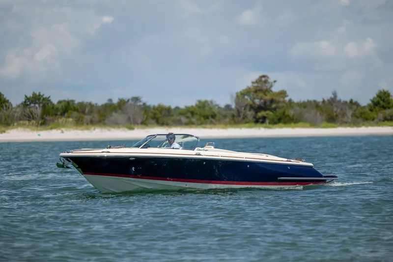 Slide: The Image of 2022 Chris-Craft Launch 27 boat cruising on calm water near a sandy shoreline. - 8