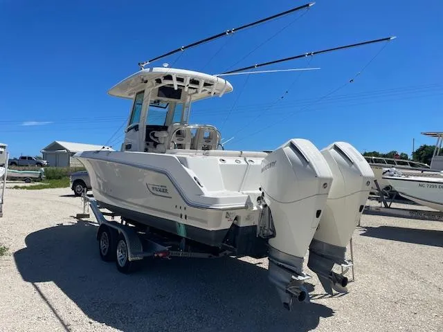 Slide: The Image of 2022 Boston Whaler 25' Outrage boat with dual engines on a trailer, under clear blue sky. - 2
