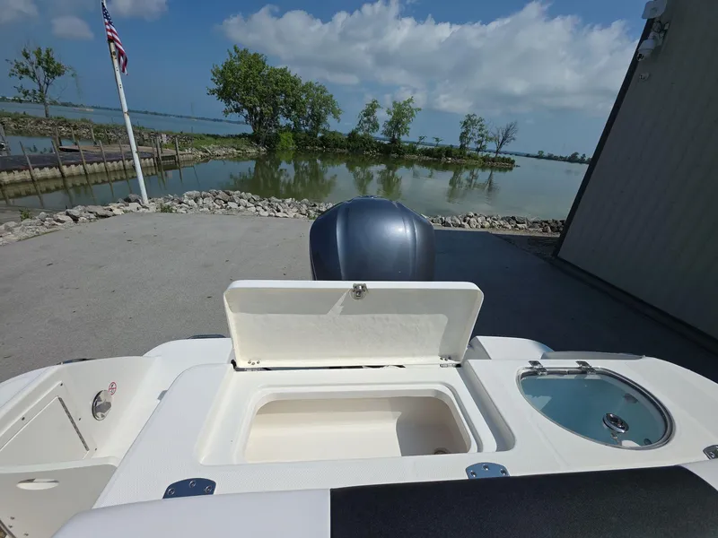Slide: The Image of 2021 Robalo R242 Center Console boat with open storage compartment, near a serene waterfront. - 17