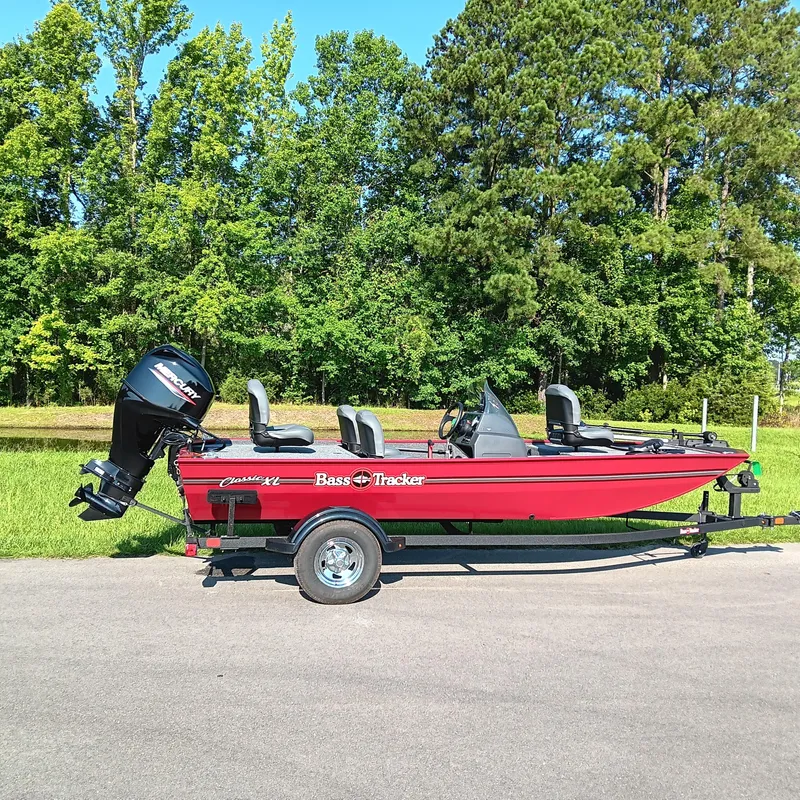 The Image of 2026 Tracker Bass Tracker Classic XL boat on trailer, parked on road with green trees in background. - 0