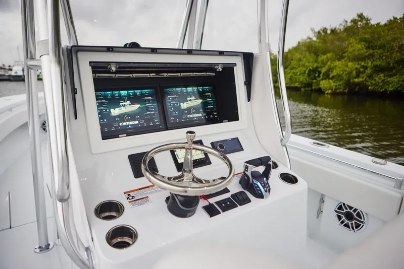 Slide: The Image of 2026 Contender 32 ST boat dashboard with dual screens and steering wheel, near lush shoreline. - 16