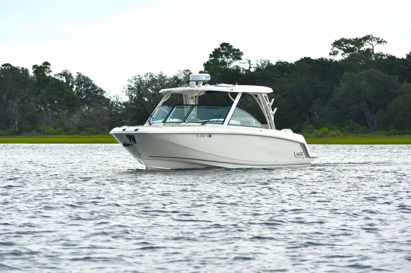 Slide: The Image of 2023 Boston Whaler 320 Vantage cruising on a serene lake with lush greenery. - 2