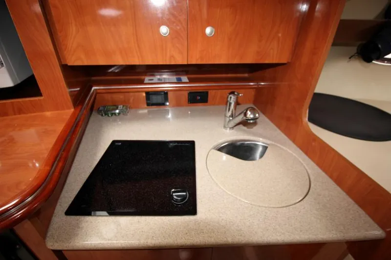Slide: The Image of 2006 Cruisers Yachts 320 Express galley with stove and sink, featuring wood cabinetry. - 23
