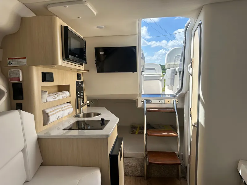 Slide: The Image of 2024 Regal 26 XO boat interior with kitchenette, TV, and ladder to deck. - 17