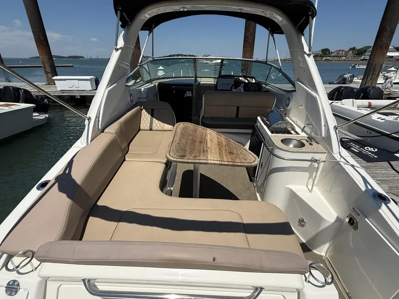 Slide: The Image of 2017 Sea Ray Sundancer 280 interior with seating, table, and kitchenette by the dock. - 11