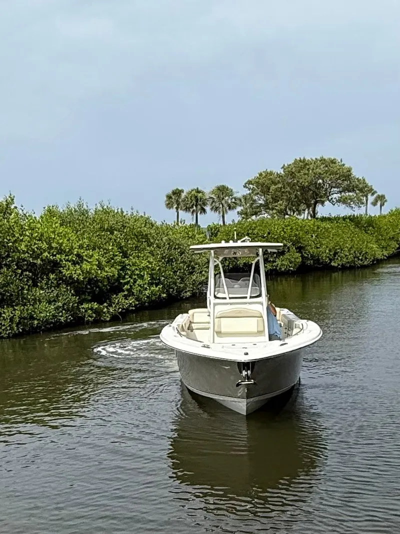 Slide: The Image of 2017 NauticStar 2602 Legacy boat navigating a narrow waterway surrounded by lush greenery. - 1