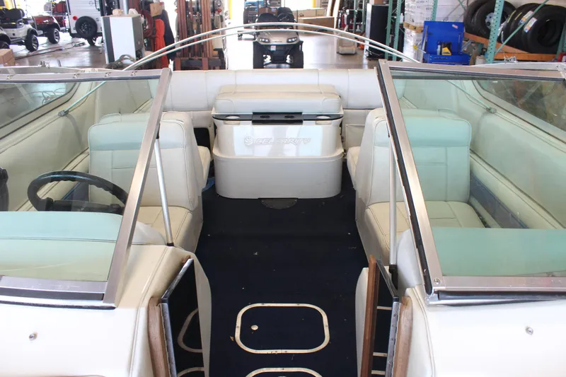 Slide: The Image of 1994 Celebrity 230 BR boat interior with white seating and steering wheel in a workshop. - 14