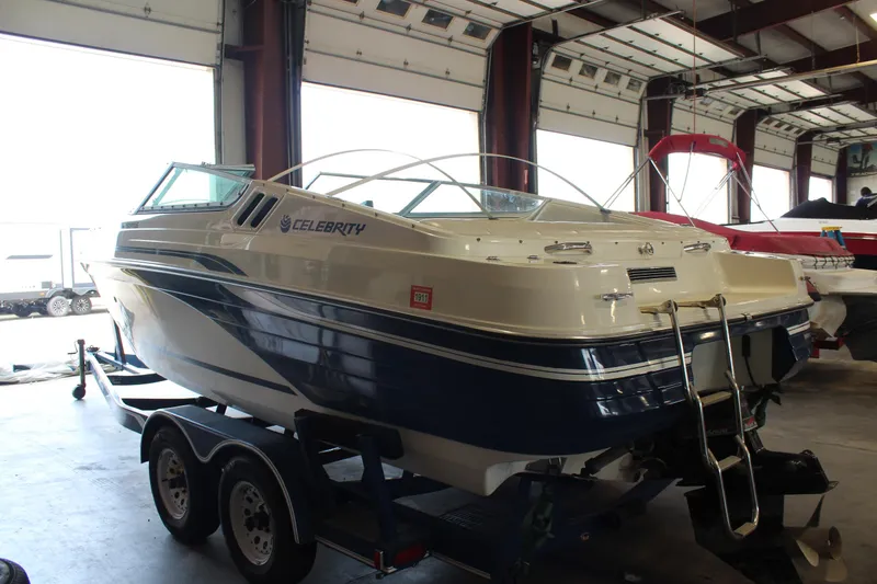 Slide: The Image of 1994 Celebrity 230 BR boat in storage, featuring a blue and white design on a trailer. - 4