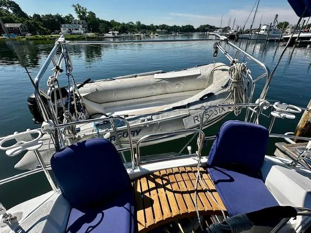 Slide: The Image of 1986 Hunter Legend 45 sailboat with dinghy on calm water, featuring blue seating and wooden deck. - 12