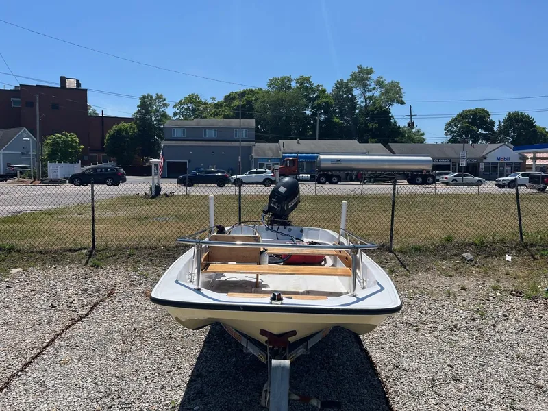 Slide: The Image of 1991 Boston Whaler 13 boat on gravel lot, with urban background and clear blue sky. - 2