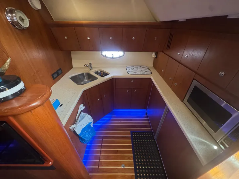 Slide: The Image of 2006 Tiara Yachts 4200 Open galley with wood cabinetry, modern appliances, and blue accent lighting. - 34