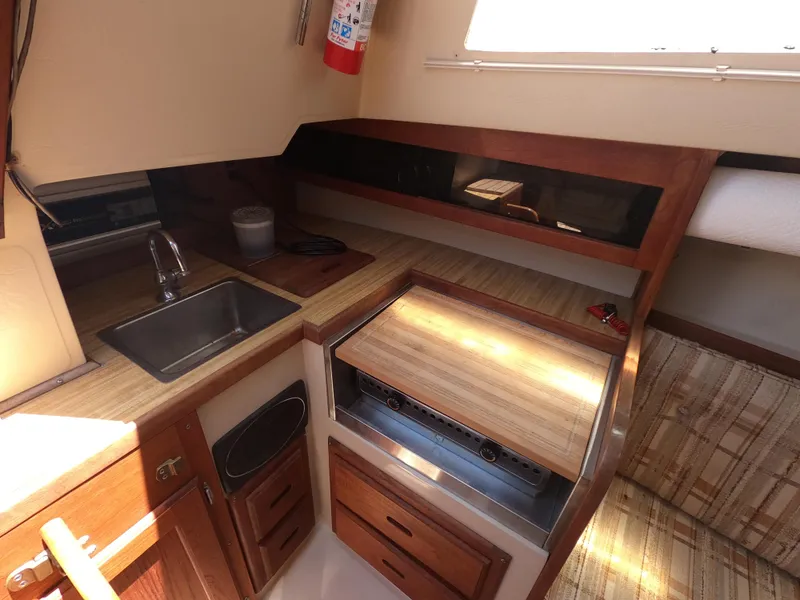 Slide: The Image of 1985 Catalina 27 yacht interior kitchen with sink, stove, and wooden cabinetry. - 13