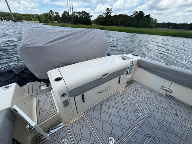 Slide: The Image of 2024 Scout 377 LXF boat interior with covered seating and storage, on a scenic waterway. - 16