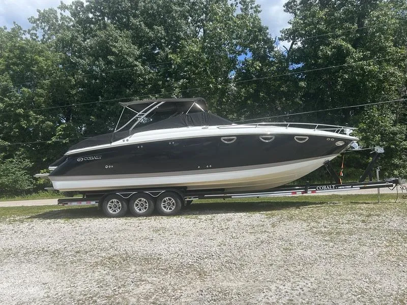 The Image of 2006 Cobalt 323 boat on trailer, parked outdoors with trees in the background. - 0