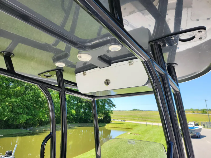 Slide: The Image of 2023 Sportsman Masters 227 Bay Boat T-top with storage compartment and lights, near a scenic waterway. - 9