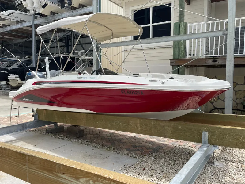 Slide: The Image of 2021 Hurricane SunDeck Sport 185 OB boat with red hull and canopy in storage. - 2