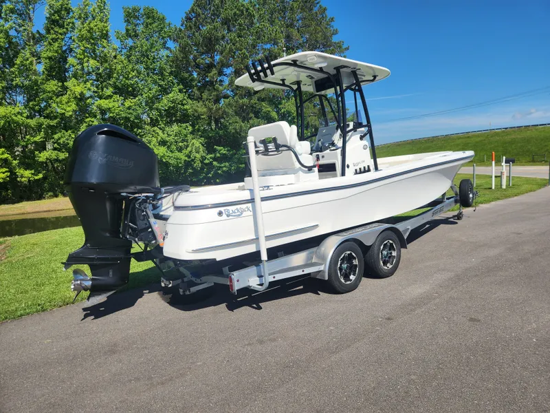 Slide: The Image of 2021 BlackJack 256 Coastal boat on trailer, parked on a sunny day near greenery. - 2