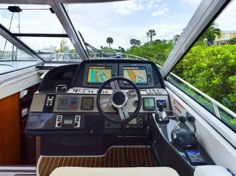 Slide: The Image of 2008 Four Winns V458 yacht helm with navigation screens and controls, docked near lush greenery. - 11