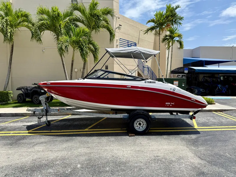 Slide: The Image of 2025 Yamaha SX195 boat in red on trailer, parked outdoors near palm trees. - 3