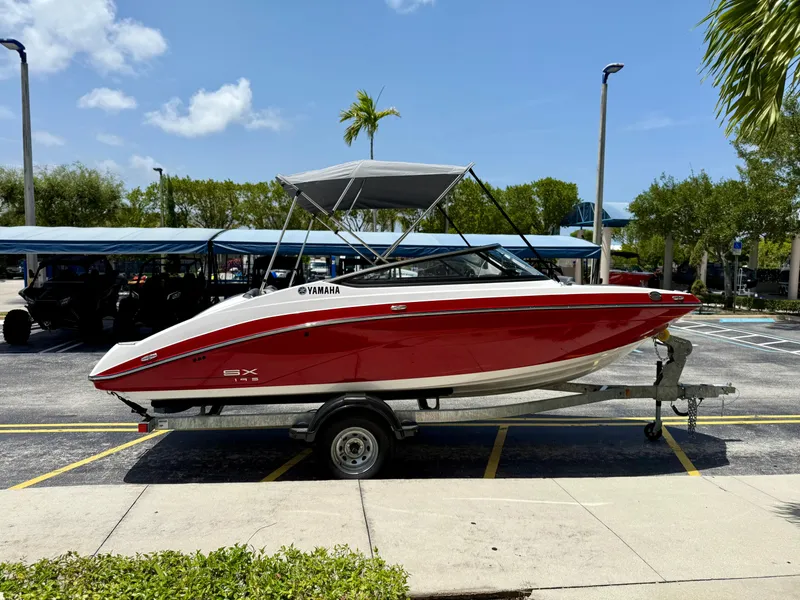 Slide: The Image of 2025 Yamaha Boats SX195 on trailer, red and white, parked outdoors under blue sky. - 7
