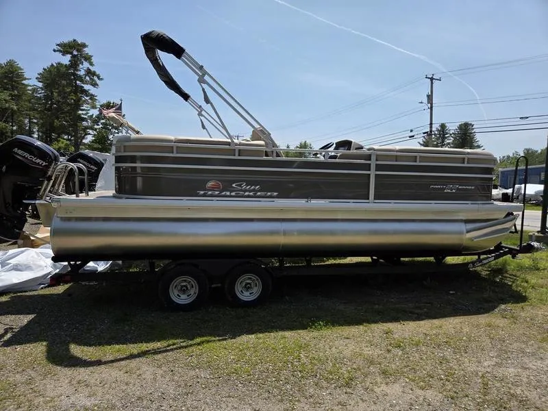 Slide: The Image of 2025 Sun Tracker PARTY BARGE® 22 DLX pontoon boat on trailer, parked outdoors. - 3