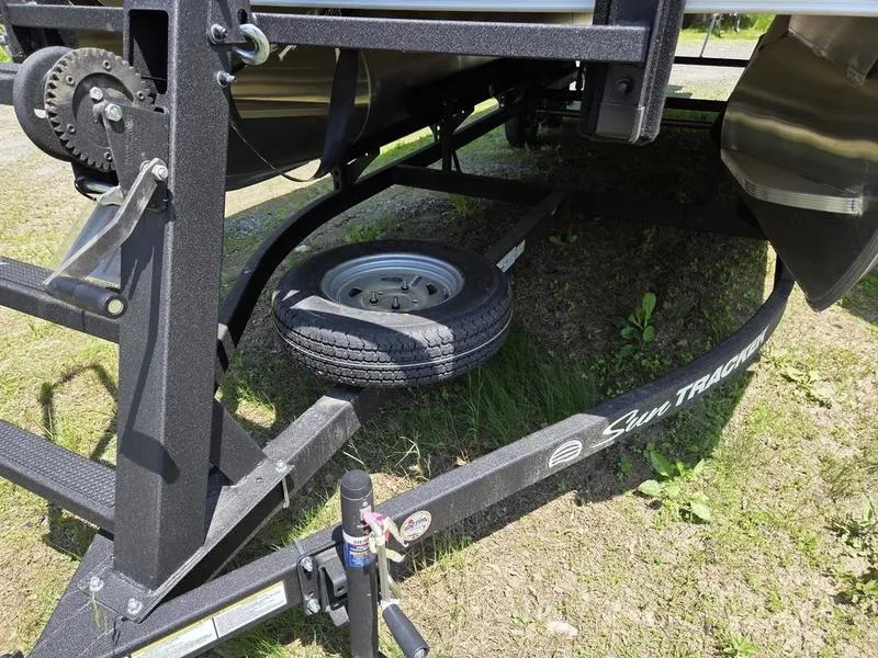 Slide: The Image of 2025 Sun Tracker PARTY BARGE® 22 DLX trailer with spare tire on grassy ground. - 5