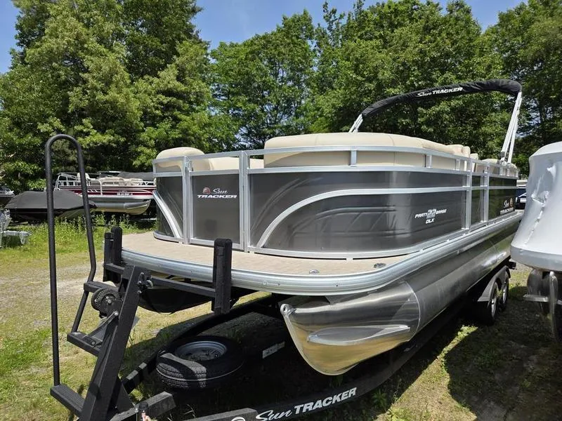Slide: The Image of 2025 Sun Tracker PARTY BARGE® 22 DLX pontoon boat on trailer, surrounded by greenery. - 7