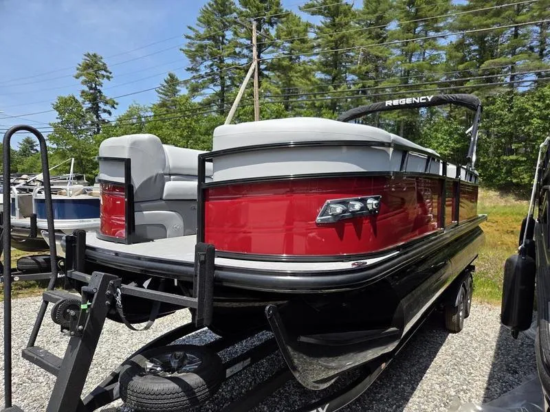 Slide: The Image of 2025 Regency 230 DL3 pontoon boat on trailer, red and gray design, parked outdoors. - 3