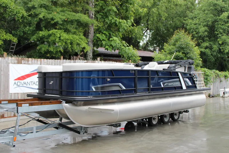 The Image of 2025 Starcraft EXS 3 DL pontoon boat on trailer, surrounded by lush greenery. - 1