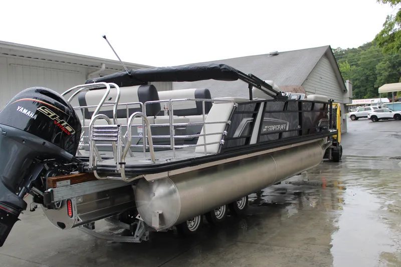 Slide: The Image of 2025 Starcraft EXS 3 DL pontoon boat with Yamaha engine, parked outdoors on wet pavement. - 4