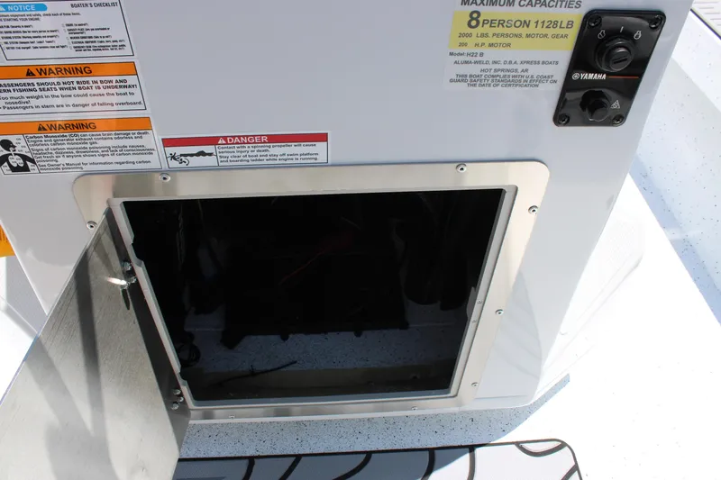 Slide: The Image of Open compartment on 2026 Xpress H22B Bay boat with warning labels and controls. - 14