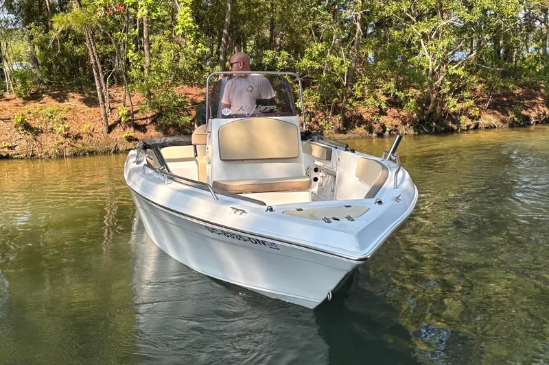 Slide: The Image of Man steering a 2019 Key Largo 2000 boat on a calm river. - 2