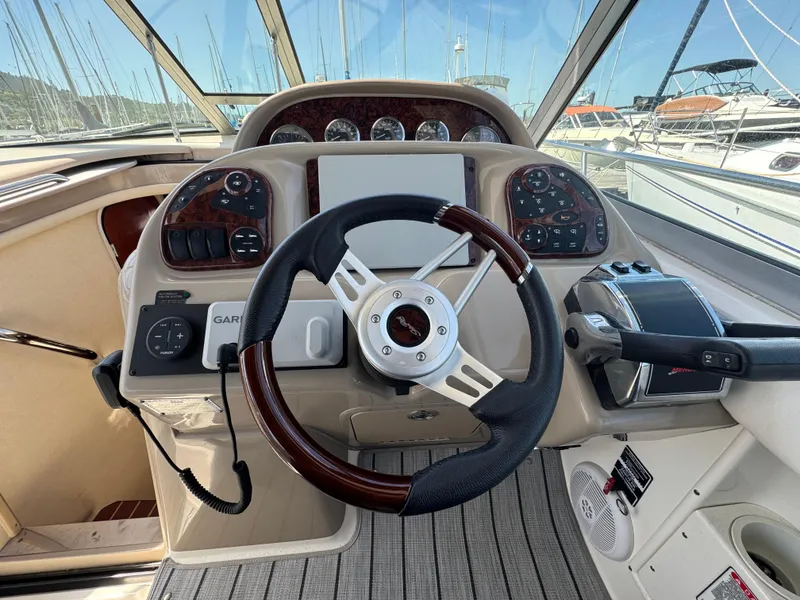 Slide: The Image of 2005 Sea Ray 300 Sundancer helm with steering wheel and control panel in marina setting. - 7