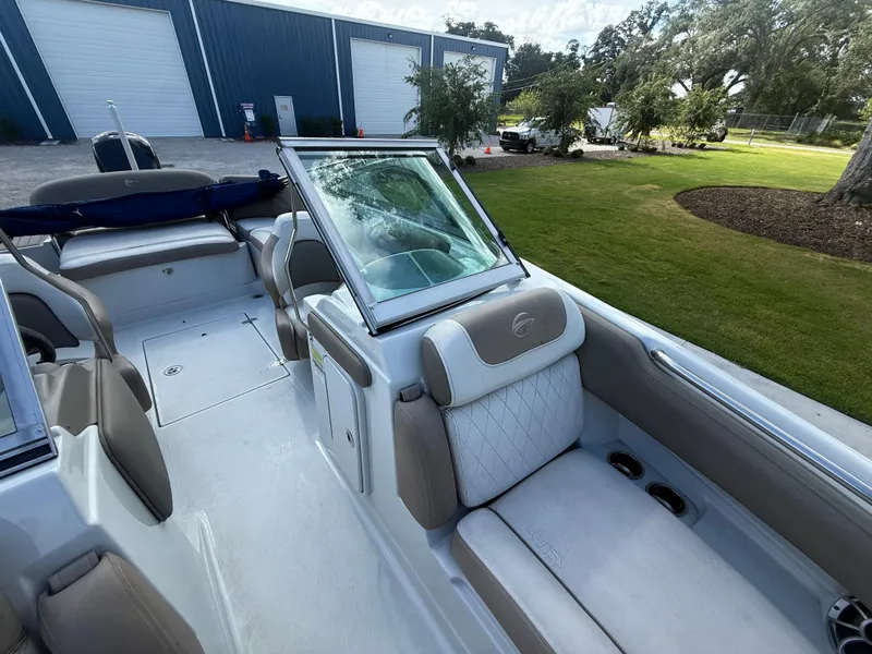 Slide: The Image of 2022 Crownline Eclipse E215 XS boat interior with beige seating, parked near a blue building. - 16