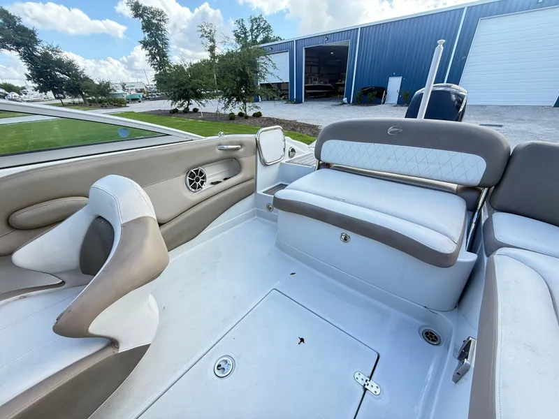 Slide: The Image of 2022 Crownline Eclipse E215 XS boat interior with beige and white seating, near a blue warehouse. - 22
