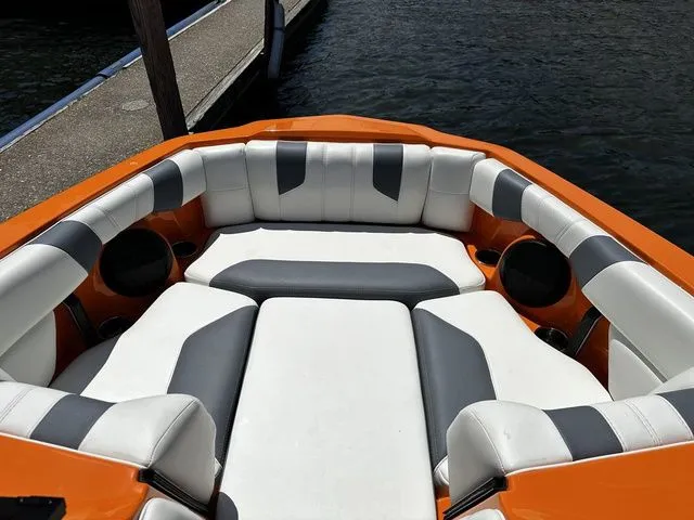 Slide: The Image of 2023 Malibu 21 LX boat interior with orange and white seating near a dock. - 18
