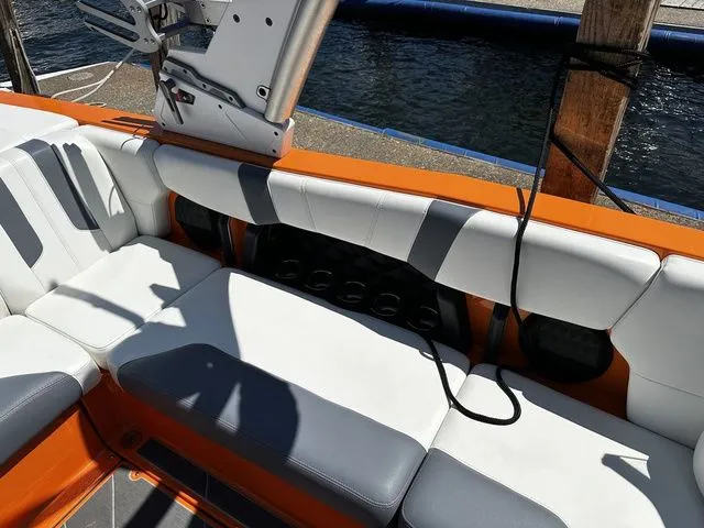 Slide: The Image of 2023 Malibu 21 LX boat interior with orange and white seating by the water. - 20