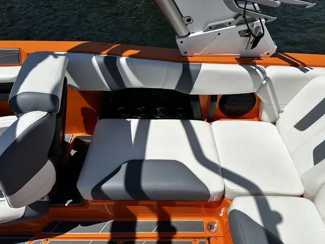 Slide: The Image of 2023 Malibu 21 LX boat interior with orange and white seating, on water. - 21