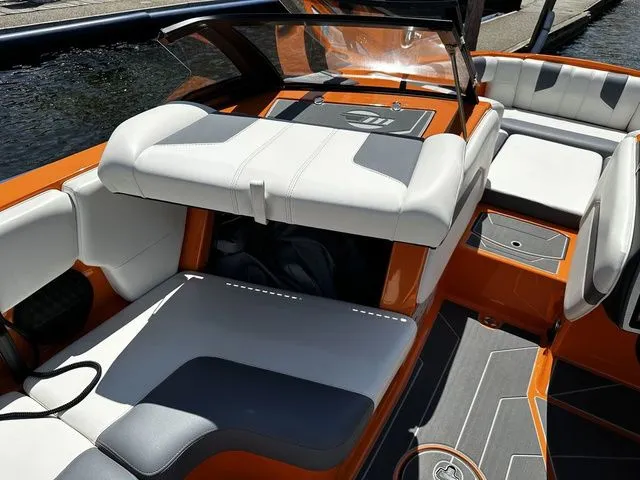 Slide: The Image of 2023 Malibu 21 LX boat interior with orange and gray seating, docked by water. - 23