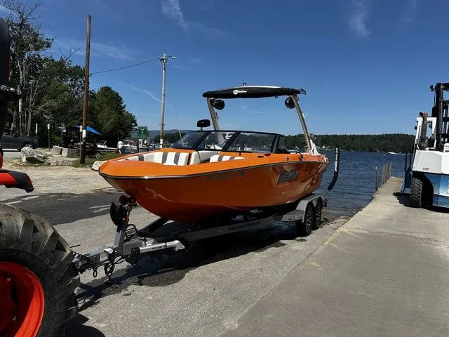 Slide: The Image of 2023 Malibu 21 LX boat in vibrant orange on a trailer by a lakeside. - 26