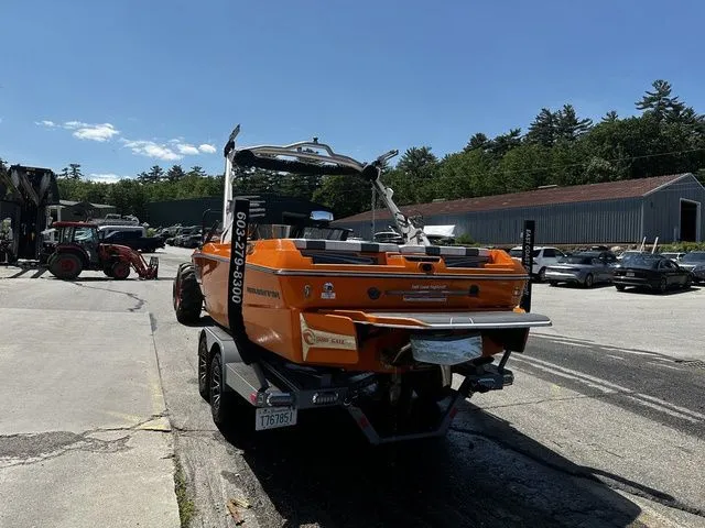 Slide: The Image of 2023 Malibu 21 LX boat in orange, parked outdoors on a trailer, sunny day. - 27