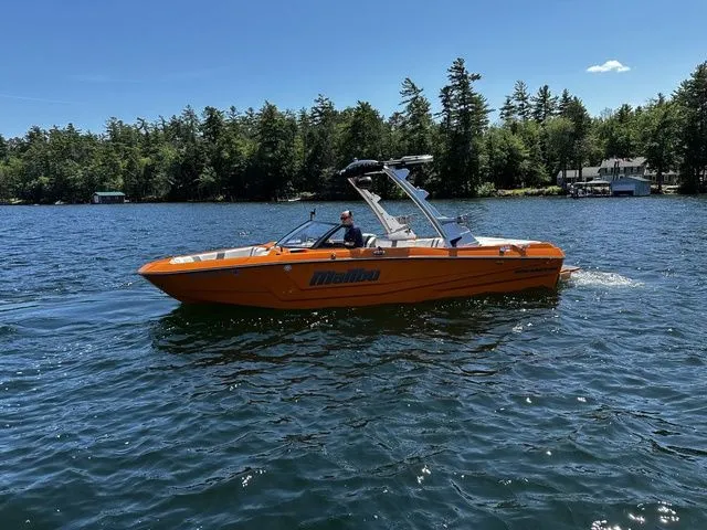 Slide: The Image of 2023 Malibu 21 LX boat cruising on a sunny lake with forested shoreline. - 4