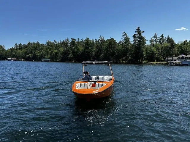 Slide: The Image of 2023 Malibu 21 LX boat on a scenic lake with forested shoreline. - 6