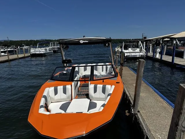 Slide: The Image of 2023 Malibu 21 LX boat docked at marina, vibrant orange exterior, sunny day. - 7