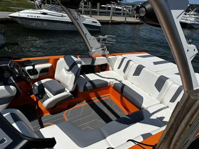 Slide: The Image of 2023 Malibu 21 LX boat interior with orange and white seating, docked by the water. - 8