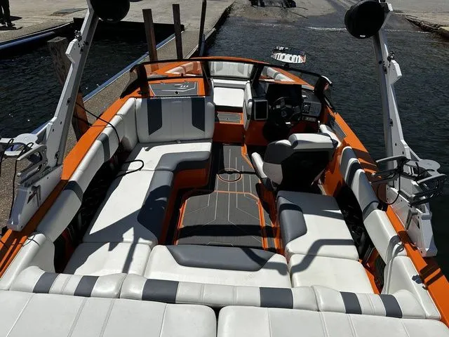 Slide: The Image of 2023 Malibu 21 LX boat interior with orange and white seating, docked by the water. - 9