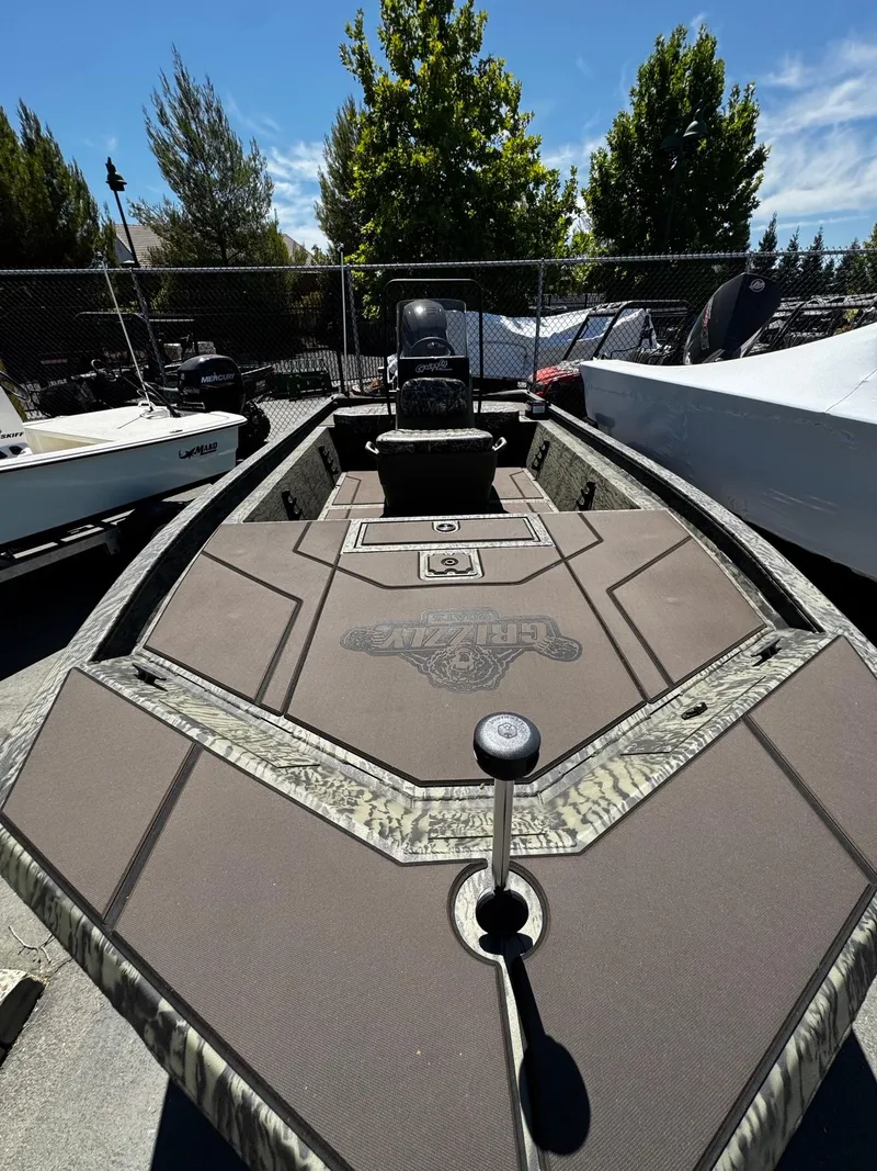 Slide: The Image of 2025 Tracker Grizzly 1860 CC boat with camouflage design, parked outdoors under clear skies. - 4