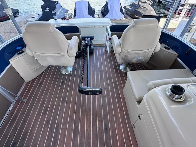 Slide: The Image of 2015 Xcursion X21F boat interior with beige seats and wood flooring, docked by the water. - 14
