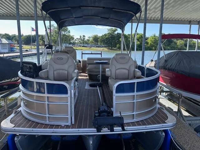 Slide: The Image of 2015 Xcursion X21F pontoon boat docked under a canopy, featuring comfortable seating and scenic lake view. - 2